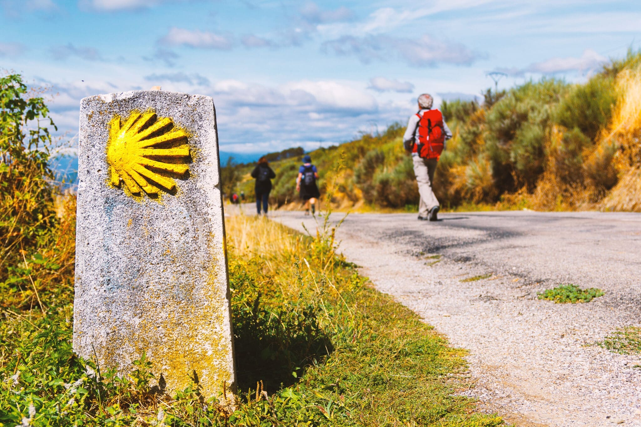 A pilgrim on the Camino beside a scallop-shell waymarker
